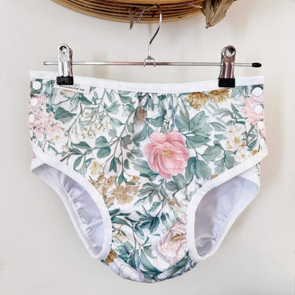 Floral print high-waisted briefs with a white waistband and leg openings, hanging from a metal hanger with black clips against a light wall.