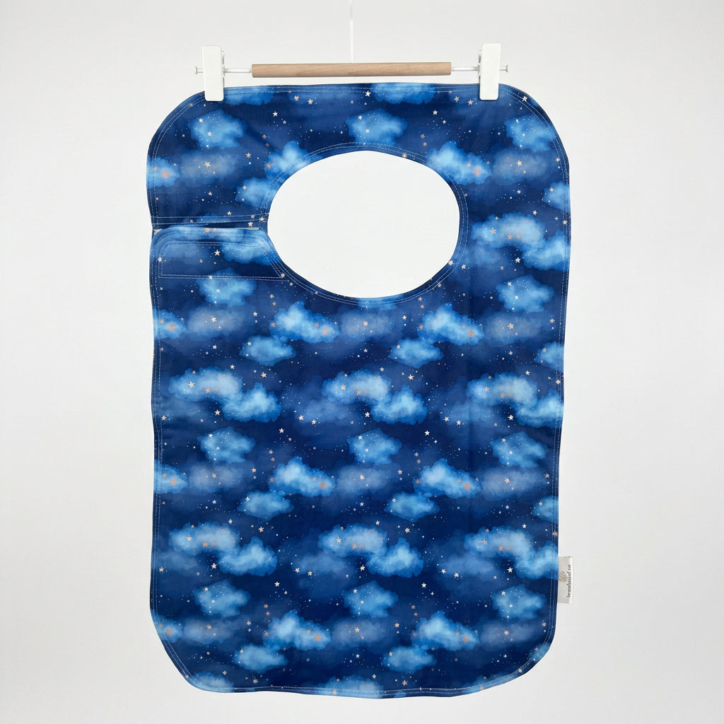 A reusable adult bib with a blue night-sky pattern featuring clouds and stars, hanging from a wooden hanger with white clips against a plain wall.