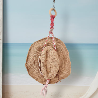 Woven hat with pink tassels hanging on a hook against a white wall
