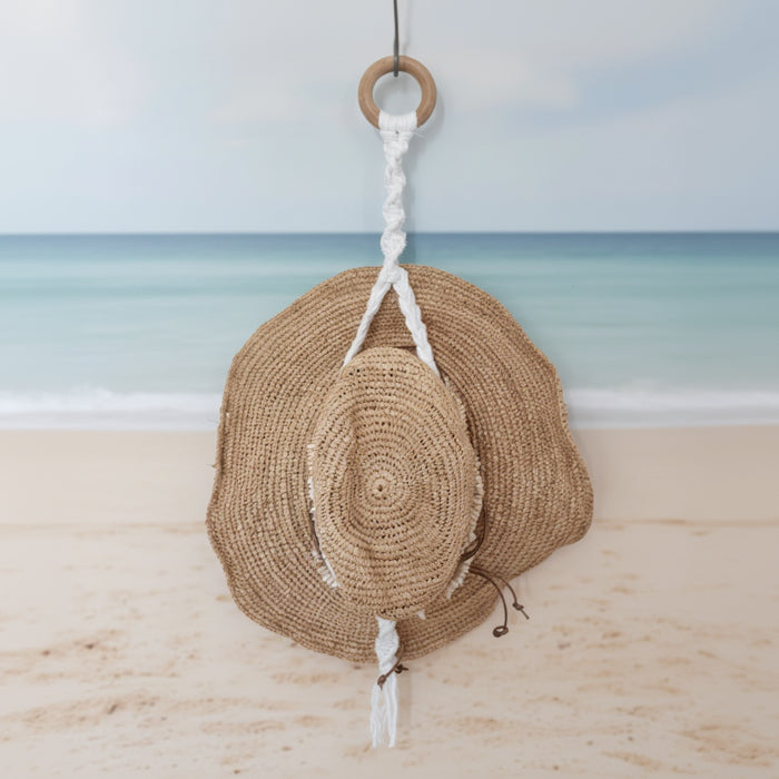 Woven hat hanging on a hook against a white wall